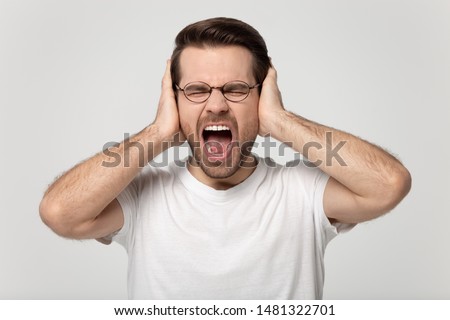 Close up headshot studio portrait young stressed mad man covering ears with hands, refusing to listen, suffering from loud noisy sounds, screaming, shouting, isolated on grey white background. Royalty-Free Stock Photo #1481322701