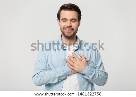 Head shot studio portrait young man with closed eyes folding crossed hands on chest near heart, isolated on grey white background. Thankful guy feeling grateful, positive emotional face expression. Royalty-Free Stock Photo #1481322758