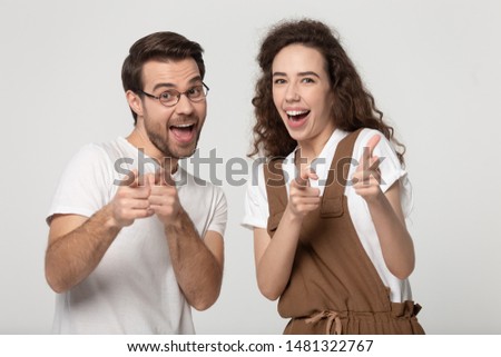 Joyful happy young family couple looking and pointing fingers at camera, isolated on grey white studio background. Cheerful young man and millennial woman appealing to you, good choice concept.