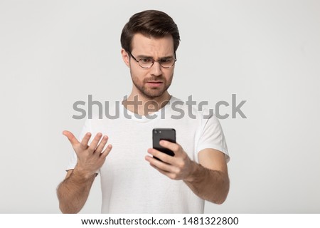 Millennial mad man annoyed by slow internet, received spam message, broken phone, troubles with shopping app, connection to wifi, looking at screen, isolated on grey white studio background. Royalty-Free Stock Photo #1481322800