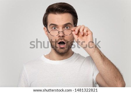 Close up head shot studio portrait young shocked surprised man looking at camera and taking off glasses, isolated on grey white studio background. Unbelievable sale discount, unexpected news concept.