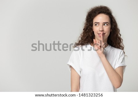 Isolated millennial girl puts finger to mouth, making hush gesture, looking aside on empty copy space for advertisement promotional text, product or service presentation, profitable secret deal.