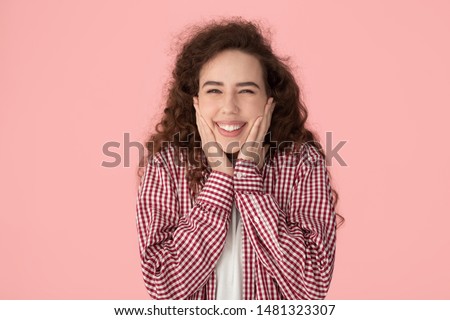 Head shot attractive happy positive millennial shy girl touching cheeks, showing healthy beautiful toothy smile, laughing, isolated on pink studio background. Young customer satisfied with service.