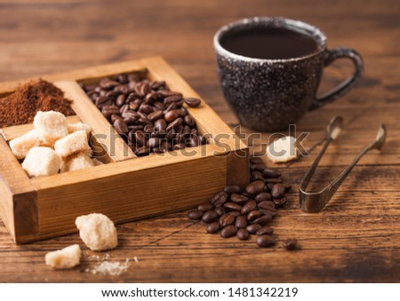 Black ceramic cup of fresh raw organic coffee with beans and ground powder with cane sugar in vintage box on wooden background.