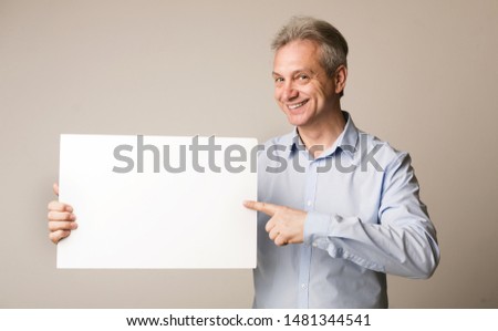 Mature man holding blank board and pointing on it, on grey background, copy space