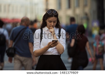 Girl on the street among the crowd of passers-by, photos in the style of surveillance. young woman in the city uses her phone to find a route, uses the Internet and mobile applications.