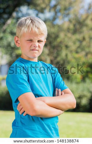 Young boy looking angry with crossed arms in the park looking at camera