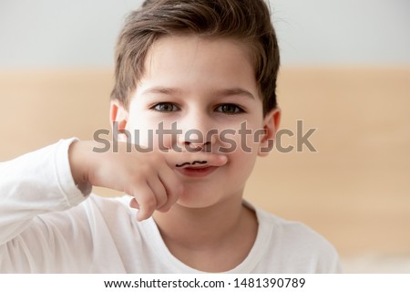 Small boy imagines himself an adult on finger drawn with black marker funny moustaches, kid framed them over lips looks alike real ones son try look older, next Generation Z, conceptual close up photo