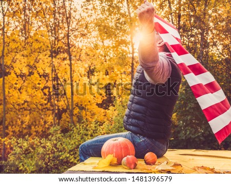 Attractive guy holding a US flag against the background of yellow trees and the setting sun. National holiday concept