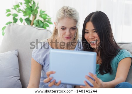 Two friends taking photo with tablet pc at home on the couch