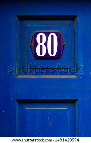 House number 80 with the eighty on a blue enamel sign on a blue wooden front door