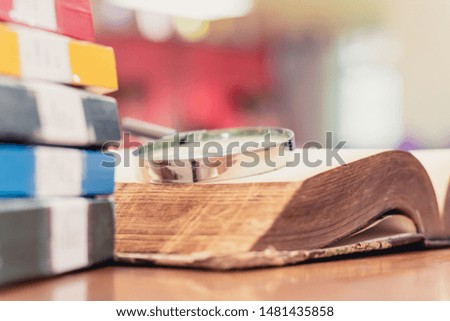 Textbook stack with magnifying glass on wooden table with blur background in library with copy space. Photo concept of education, knowledge, traditional learning, and literature. Selective Focus