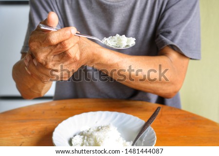 Elderly man is holding his hand while eating because Parkinson's disease.Tremor is most symptom and make a trouble for doing activities such as eat.Health care or elderly concept.Front view. Royalty-Free Stock Photo #1481444087