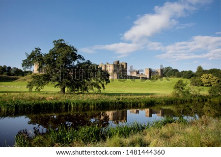 Alnwick Castle in Northumberland and is pictured here reflected in the River Aln on a bright August morning. The castle dates from 1096 and is more recently featured in the Harry Potter films