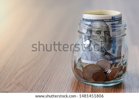 US dollar banknote and coins into glass jar.on wooden table.Collecting and saving for future investment concept.