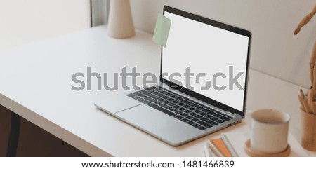 Minimal comfortable room with open blank screen laptop and office supplies on white wooden table 