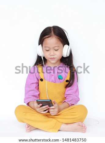 Smiling little girl enjoys listening to music by headphones isolated over white background.
