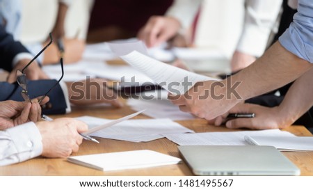 Close up of diverse businesspeople brainstorm discussing paperwork share project ideas together, employees gather consider financial paper handout material, company statistics at office briefing Royalty-Free Stock Photo #1481495567
