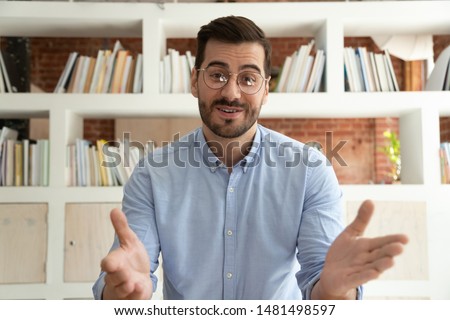 Smiling young businessman sit at desk talk on webcam having video call or conversation with client, motivated millennial male coach or trainer speak shoot online tutorial, record training course Royalty-Free Stock Photo #1481498597
