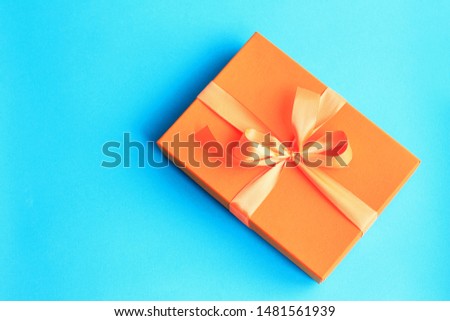 Orange craft paper gift with orange ribbon on dark blue background with copy space.