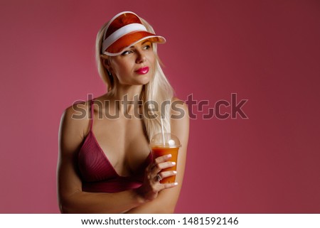blonde girl in a bathing suit and hat holding a cocktail in her hands on a pink background. woman drinks fresh juice. healthy life