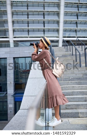 Girl photographer in a hat and with a backpack takes pictures in the city