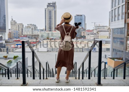 Girl photographer in a hat and with a camera looks at the city landscape