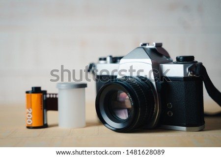 Old SLR film camera and a roll of film on wooden background.