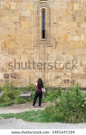 Girl photographs gravestones of old graves near the stone wall of an old church