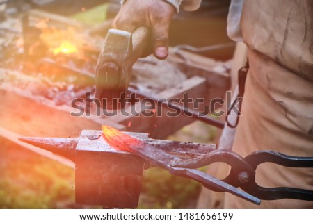 The blacksmith has a hammer on hot iron. The workpiece is clamped in the grip of the master. Bellows with fire on the background of handicraft work.