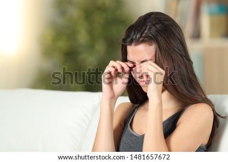 Girl suffering itching scratching eyes sitting on a couch in the living room at home Royalty-Free Stock Photo #1481657672