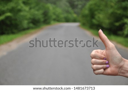 Female hand shows thumb on the background of the road. Hitchhiking on the road.
