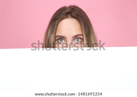 Beautiful young woman holding white blank board on pink background