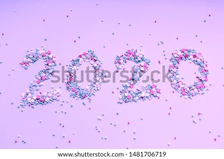 Symbol from numbers 2020 made of colored confetti laying on pink paper background. New year concept. Flat lay.