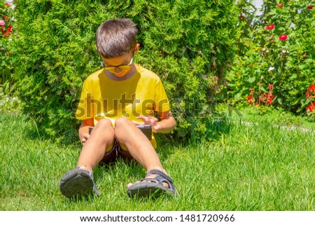 Preteenage Boy reading ebook on a gren grass
