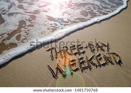 Three-Day Weekend message handwritten on smooth sand beach with lens flare above an incoming wave Royalty-Free Stock Photo #1481750768