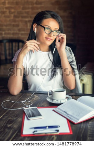 Beautiful smiling woman in glasses is listening music by her smartphone at cafe. Lifestyle concept