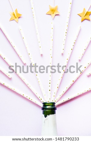 Creative photo of champagne bottle  on pink background with  celebrative toothpick  and straws.Flat lay of christmas, anniversary, new year celebration.