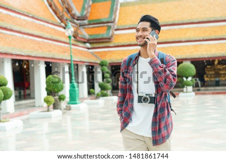 Asian man tourist walking talk smart phone and smile at Wat Suthat Thepwararam Ratchaworawihan Bangkok, Thailand in the summer time, Solo travel and backpacker concept