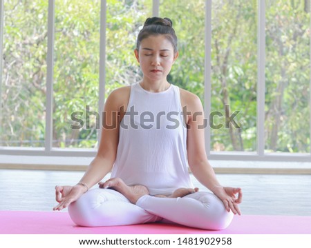 Asian women are practicing yoga. Put on white clothes in the indoor. Yoga is to practice meditation and determine breath. Health fitness concept