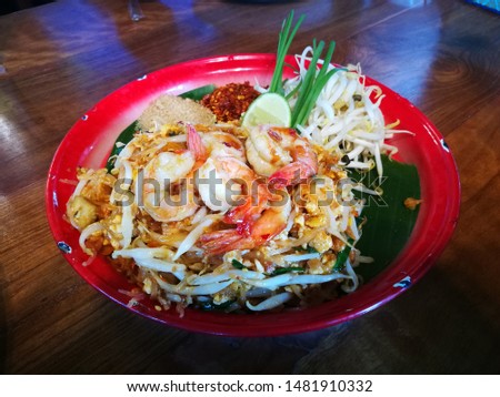 Fried Rice Sticks with Shrimp on banana leaves in a red dish. And have bean sprouts, lemon, cayenne and sugar. This is a Thai food picture.