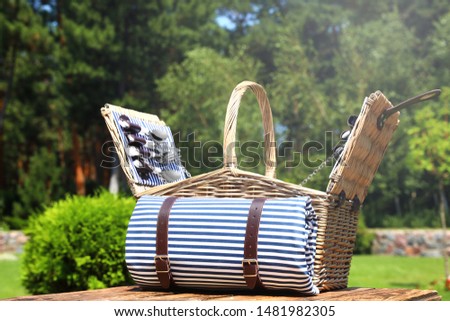 Picnic basket with blanket on wooden table in garden