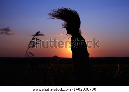 Silhouette of a girl who dances in a field on a sunset background.