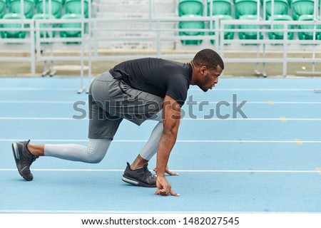 muscular runner standing in the croach, low start at the stadium. full length side view photo. copy space