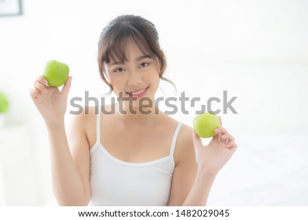 Beautiful portrait young asian woman holding and eating green apple fruit in the bedroom at home, lifestyle of nutrition girl healthy and care weight loss, health and wellness concept.