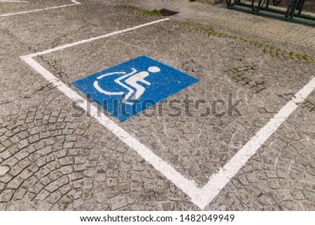 Accessible parking space reserved for persons with disabilities. Blue square with a person in a wheelchair painted on a cobblestone pavement of the old town of Salzburg, Austria.