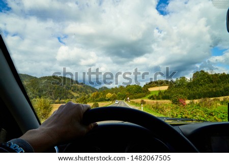 Track from the car window and white clouds on blue sky. Woman's hand on the steering wheel. Female driver seeing beautiful autumn landscape during travel in auto
