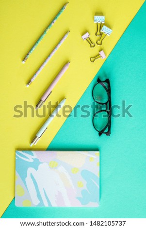 Overview of pens, clips, notebook and eyeglasses on yellow and blue background