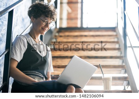 Pretty designer in casualwear sitting on staircase with laptop on her knees
