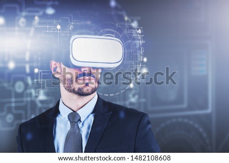 Bearded caucasian man in suit wearing VR glasses with double exposure of HUD hi tech interface. Concept of modern technology. Toned image blurred